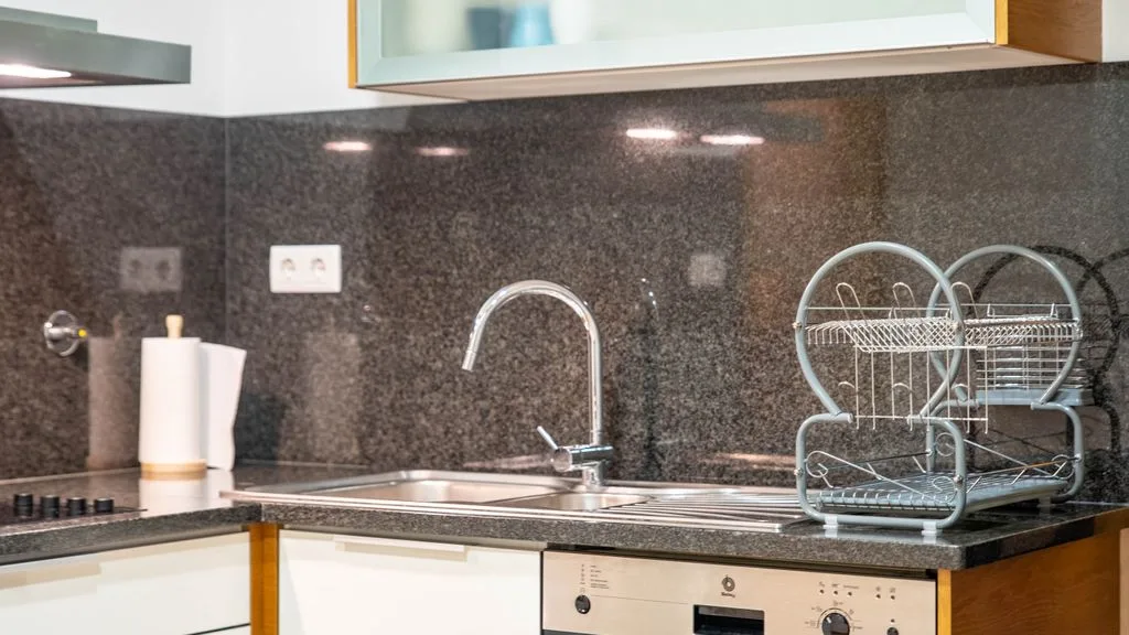 A kitchen counter with a sink, faucet, and dish rack.