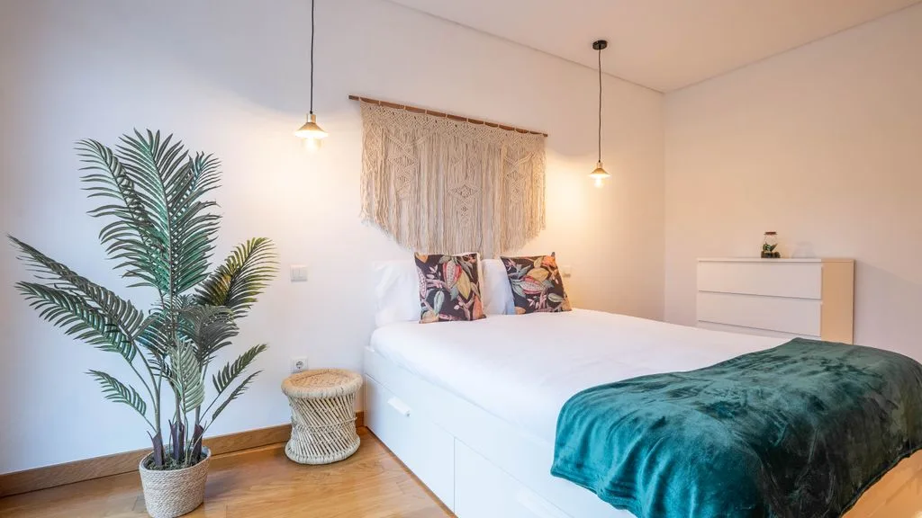 A bright bedroom with a white bed, patterned pillows, and a teal blanket.