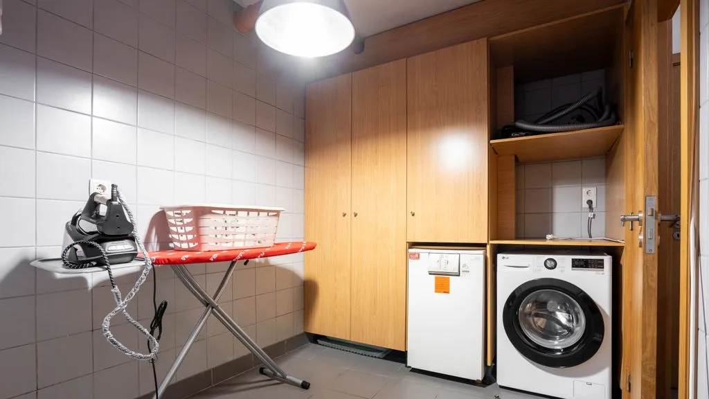 A tiled laundry room with a washing machine, dryer, and ironing board.