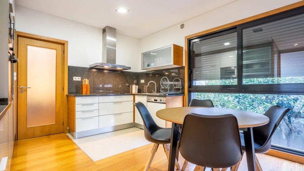 A bright kitchen and dining area with a table beside large windows.