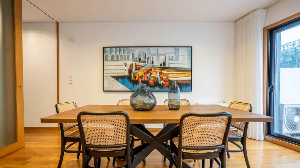 A dining area with a wooden table, woven chairs, and a framed painting.