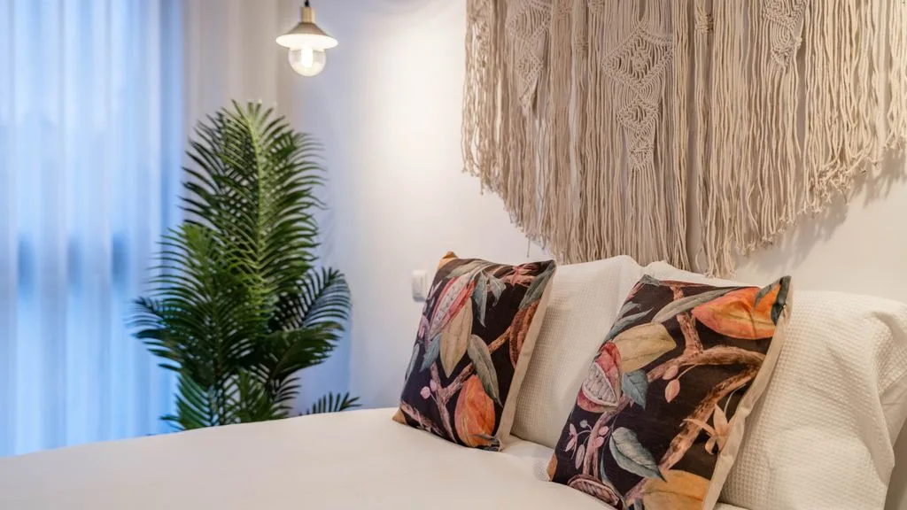 A bedroom with a bed, patterned pillows, and a leafy plant beside the window.