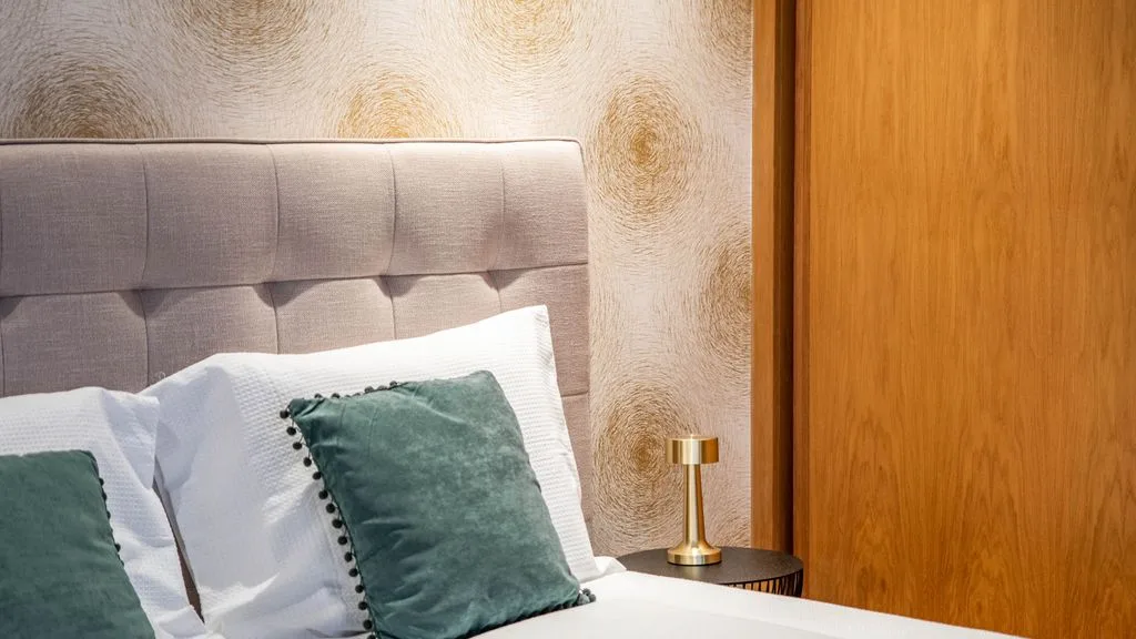 A bedroom with a padded headboard, white bedding, and green accent pillows.