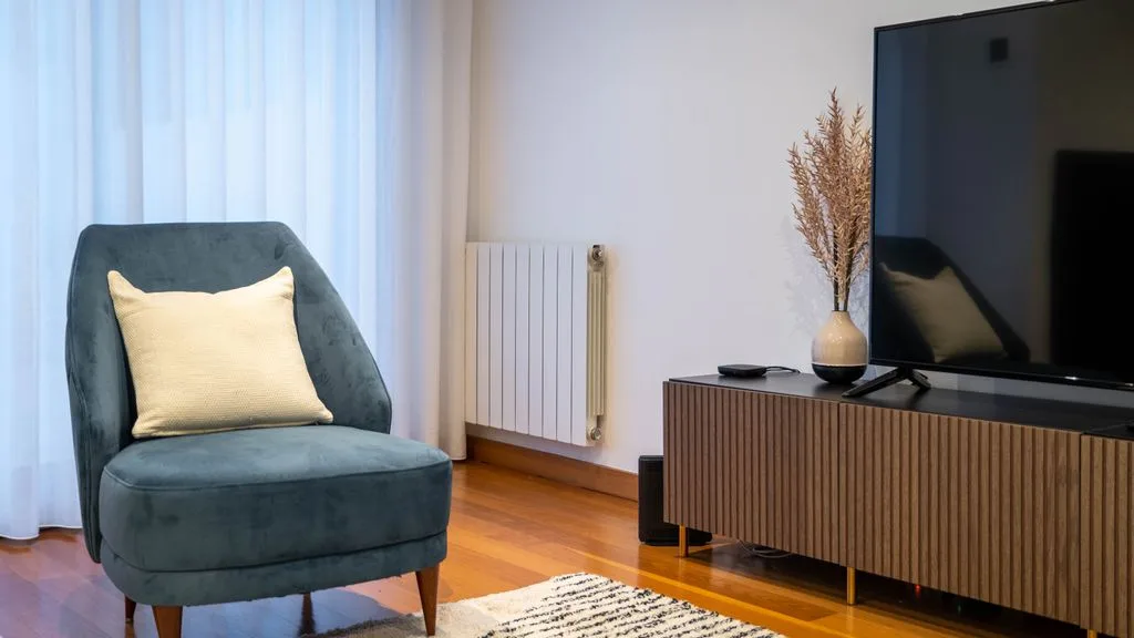 A living room with a cushioned seat, television, and wooden media console.