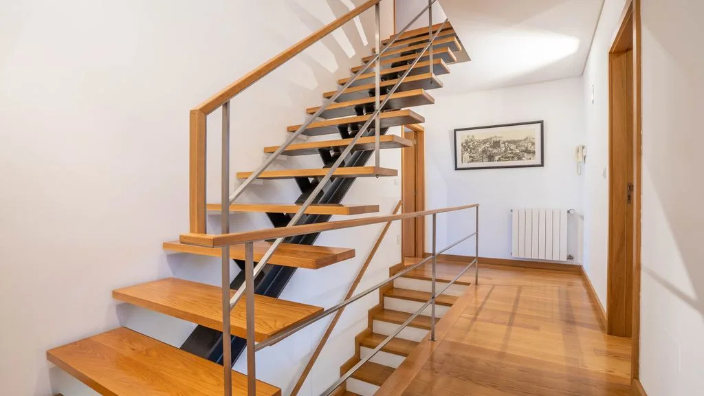 An indoor hallway with a wooden staircase and a framed picture on the wall.