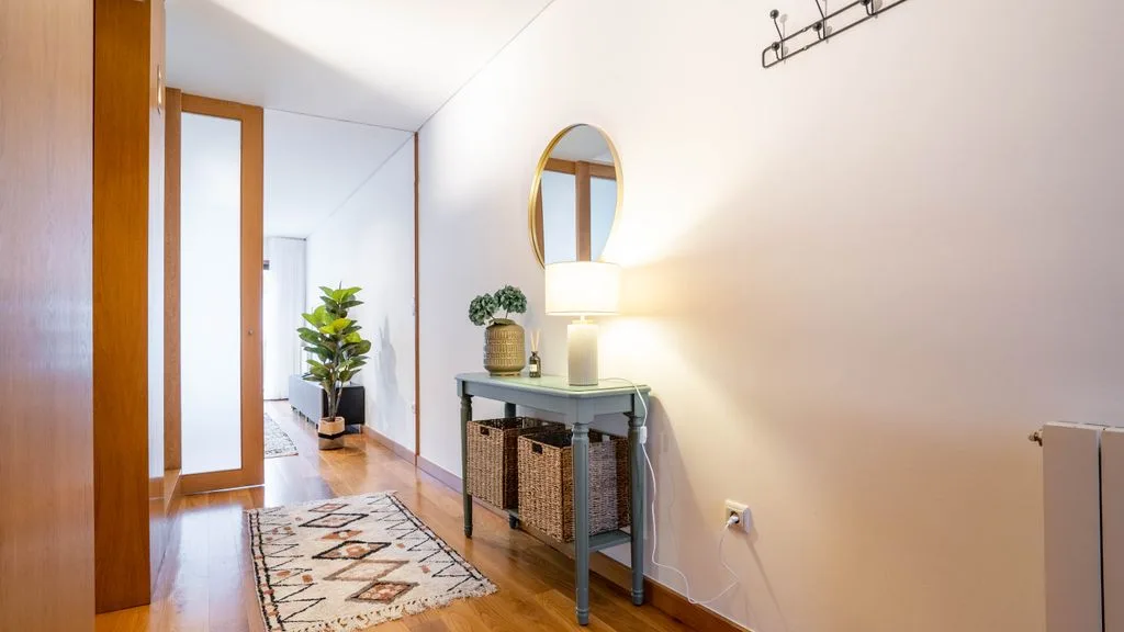 A hallway with a console table, oval mirror, and patterned runner.
