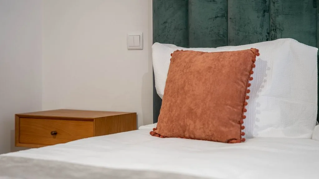 A bedroom with white bedding and a rust-colored cushion.