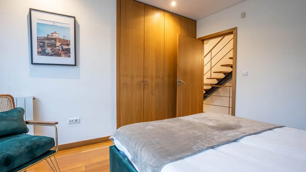 A bedroom with a bed, wooden wardrobe, and a framed picture on the wall.