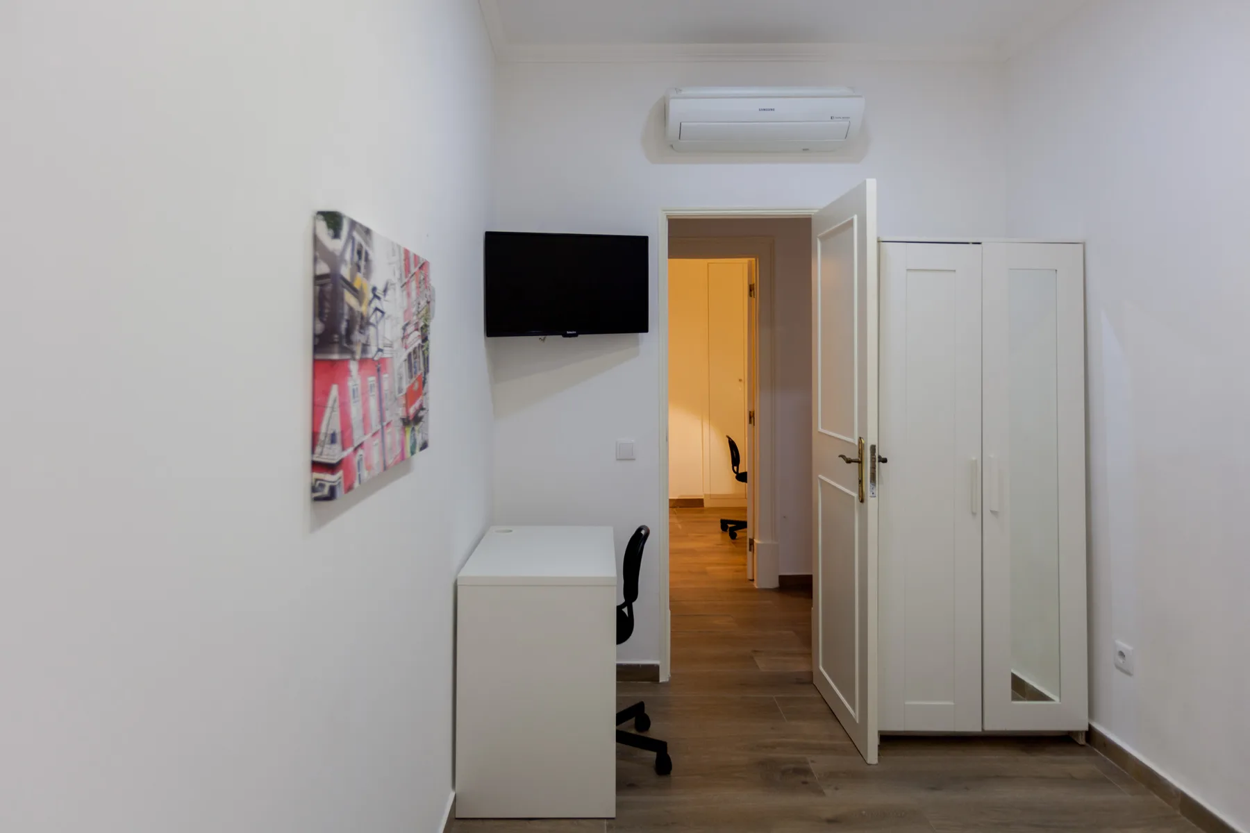 A bedroom with a desk, wall-mounted television, and open doorway.