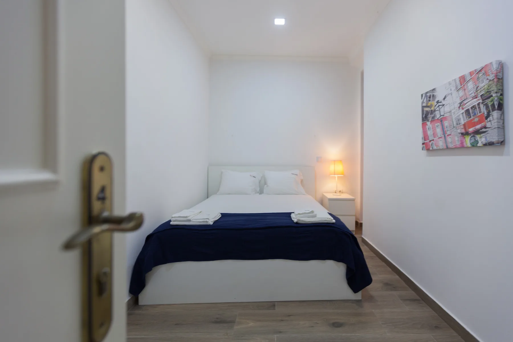 A bedroom with a neatly made bed, bedside lamp, and framed artwork.