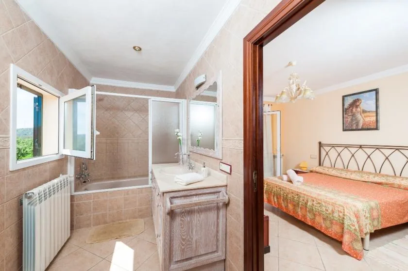 A tiled bathroom with a sink and window opens onto a bedroom.