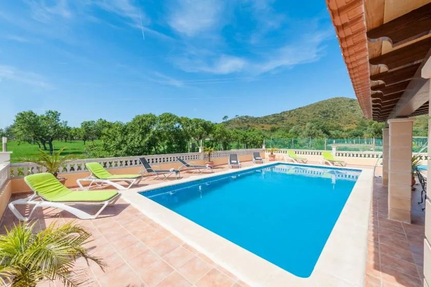 An outdoor swimming pool is surrounded by lounge seating and a tiled patio.
