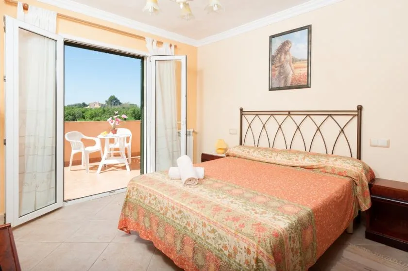 A bedroom with a bed beside open doors leading to a balcony.