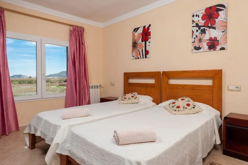 A bedroom with two beds, floral wall art, and a window with pink curtains.