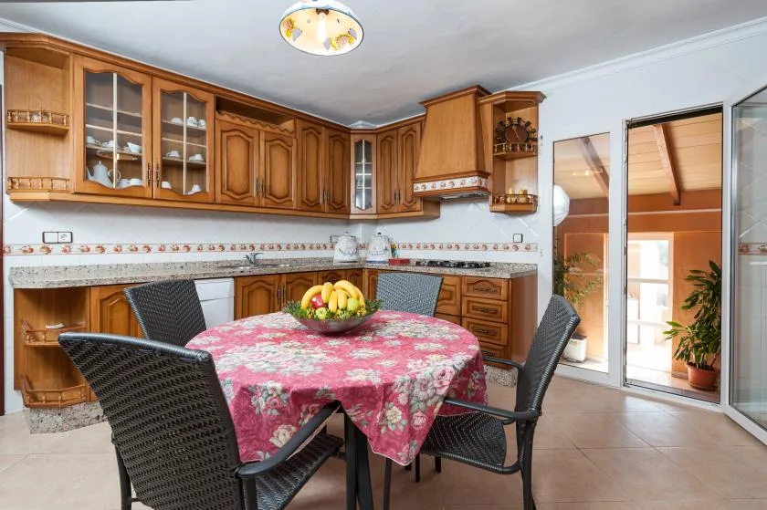 A dining area with a round table covered by a floral cloth and surrounding seating.