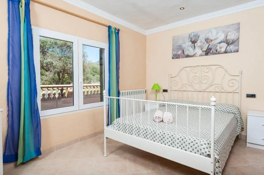 A bedroom with a white metal bed beside windows with blue curtains.