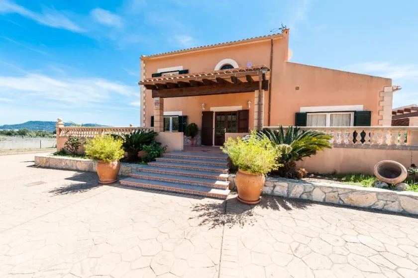 A peach-colored house entrance opens onto a paved courtyard with potted plants.
