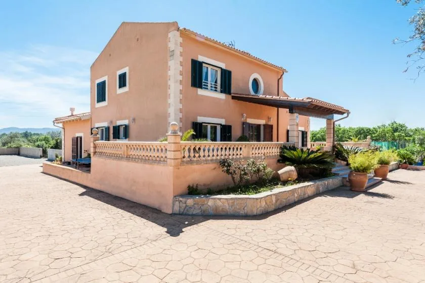 A peach-colored house stands beside a paved courtyard, with plants along the terrace.