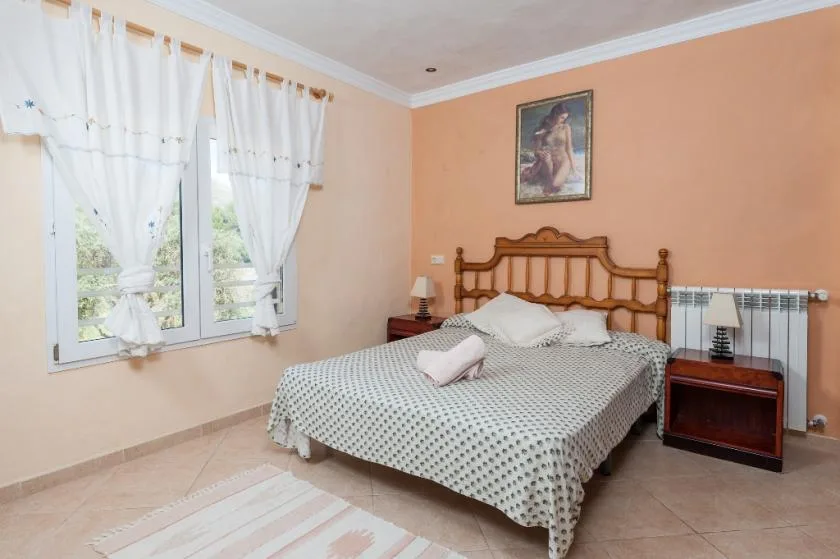 A bedroom with a wooden bed, patterned bedding, and a window with white curtains.