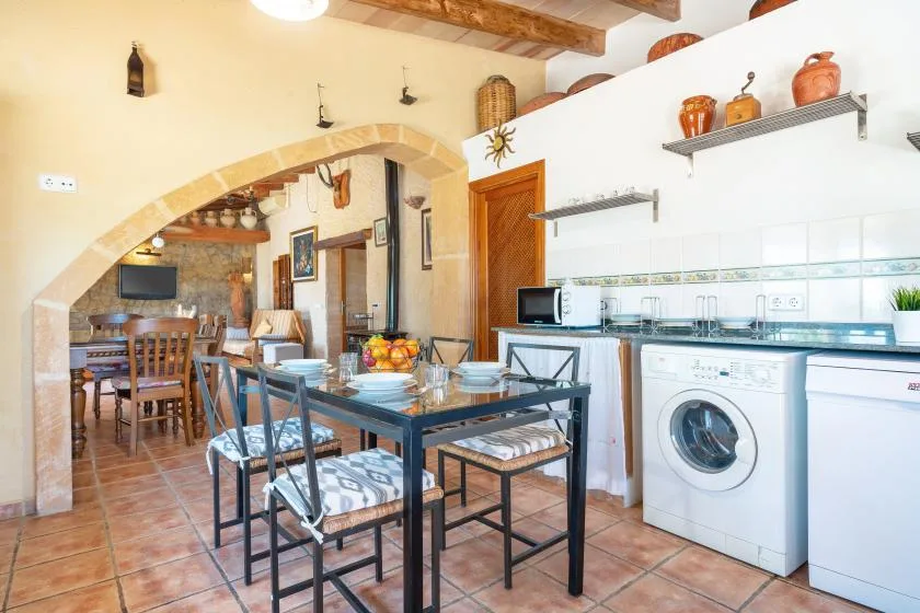 A dining area beside a kitchen, with a glass-topped table and laundry appliances.