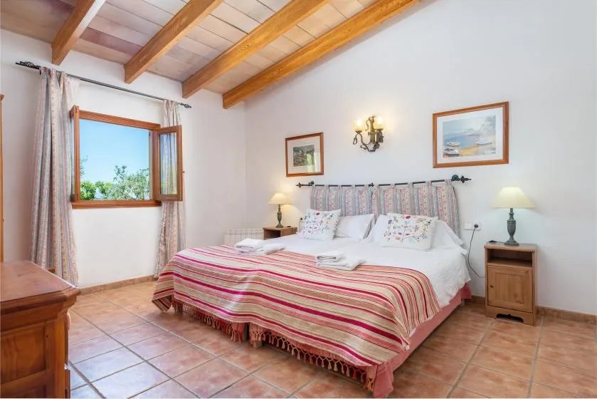 A bedroom with a double bed, striped bedspread, and exposed wooden ceiling beams.