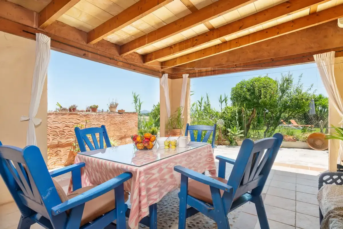 A covered patio has a dining table and blue seating overlooking a garden.