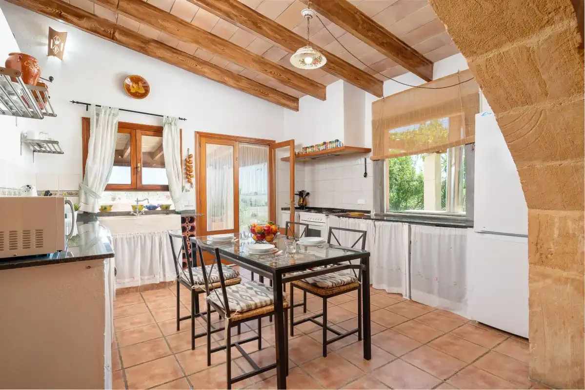 A kitchen and dining area with a table beneath exposed wooden ceiling beams.