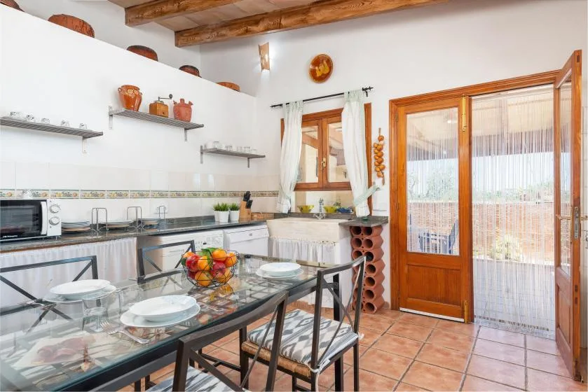 A kitchen and dining area with a glass-topped table beside an open doorway.