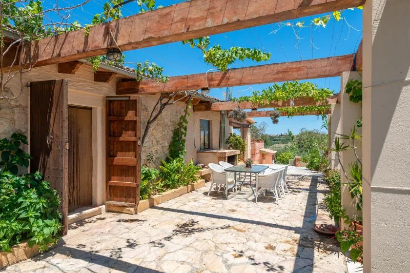 An outdoor patio with a dining table and chairs beneath wooden beams.