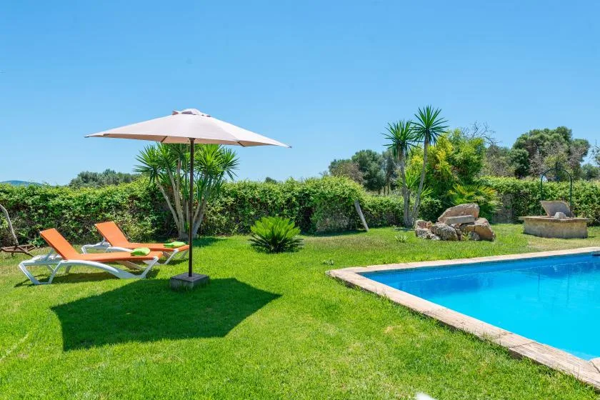 A garden pool beside a lawn with loungers and a sun umbrella.