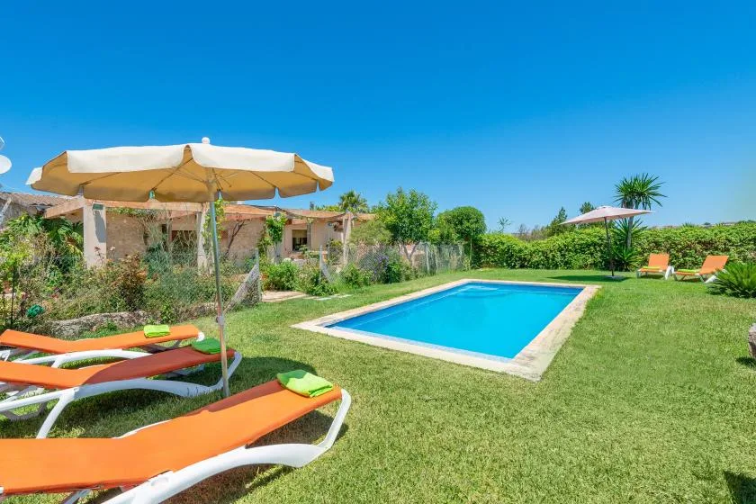 A garden swimming pool is surrounded by green lawn and orange sun loungers.