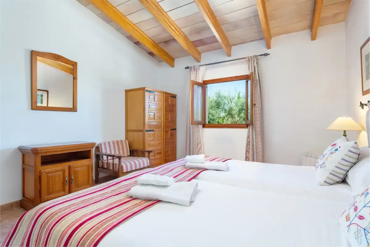 A bright bedroom with white bedding, striped blankets, and exposed wooden ceiling beams.