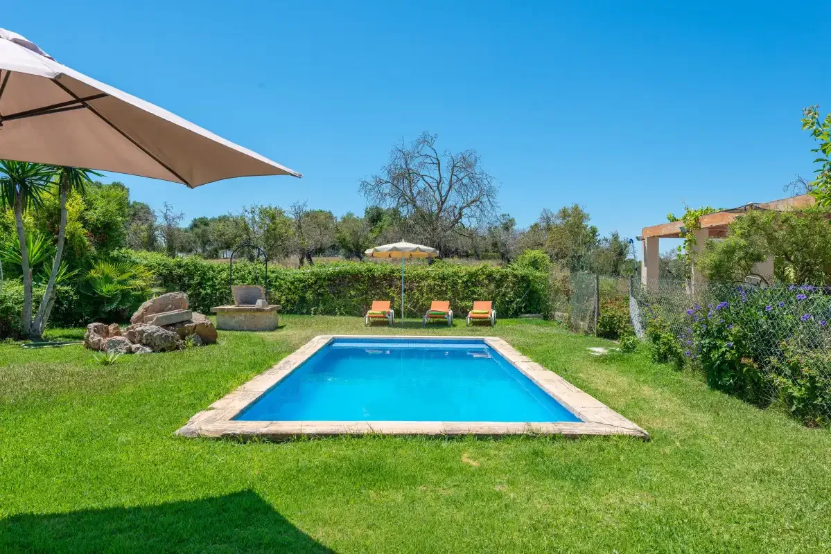 A garden swimming pool sits in a lawn, with lounge seating beyond it.