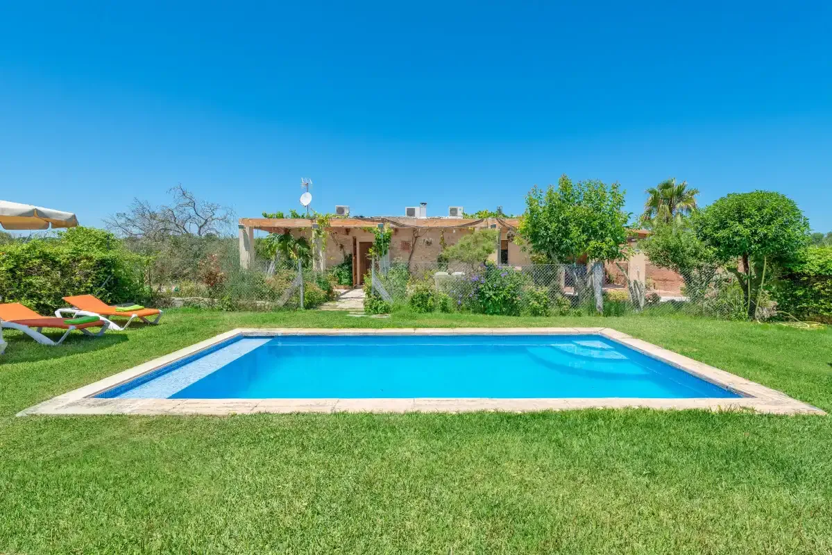 A swimming pool sits in a grassy garden beside a low house.