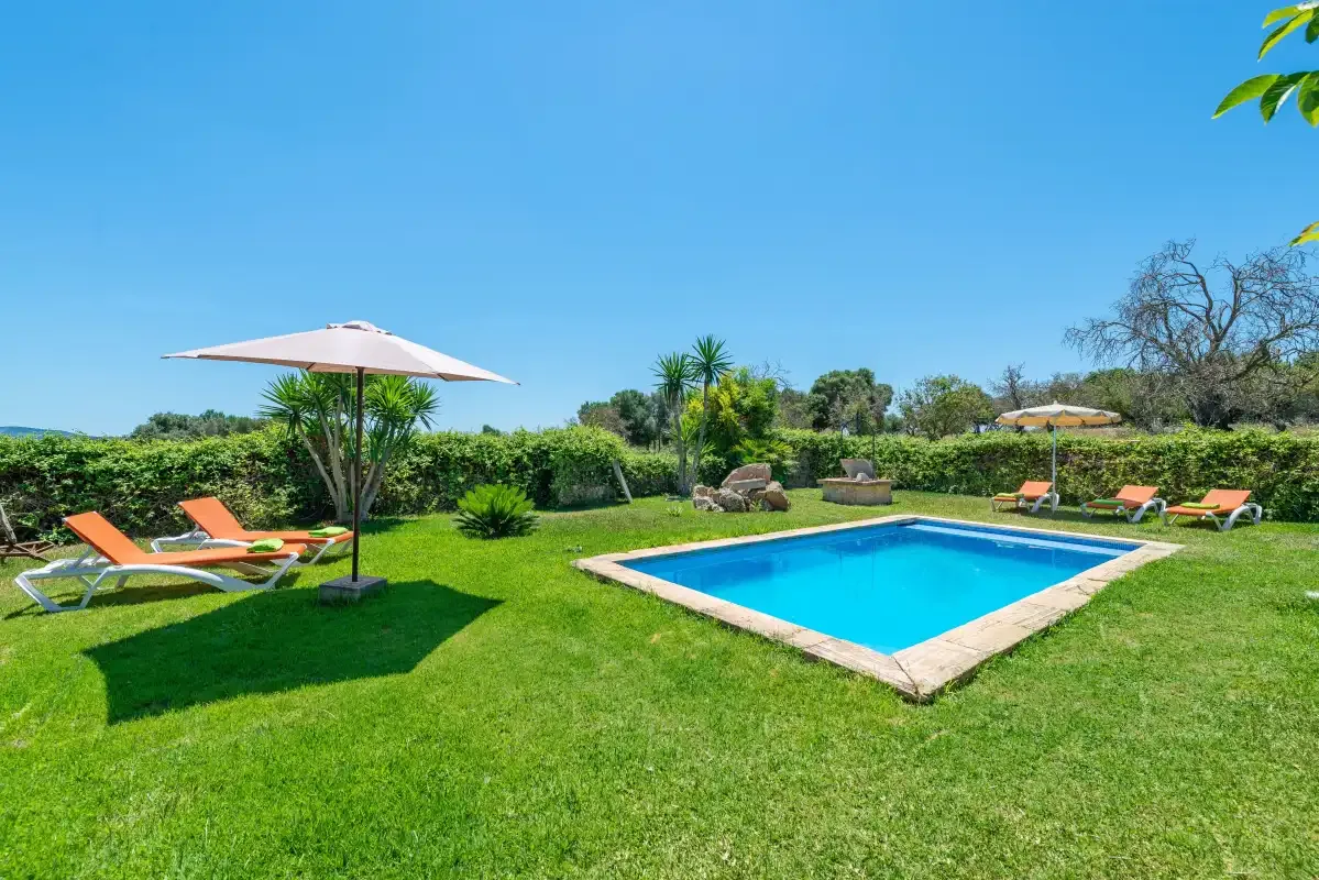 An outdoor swimming pool sits in a grassy garden with sun loungers and an umbrella.