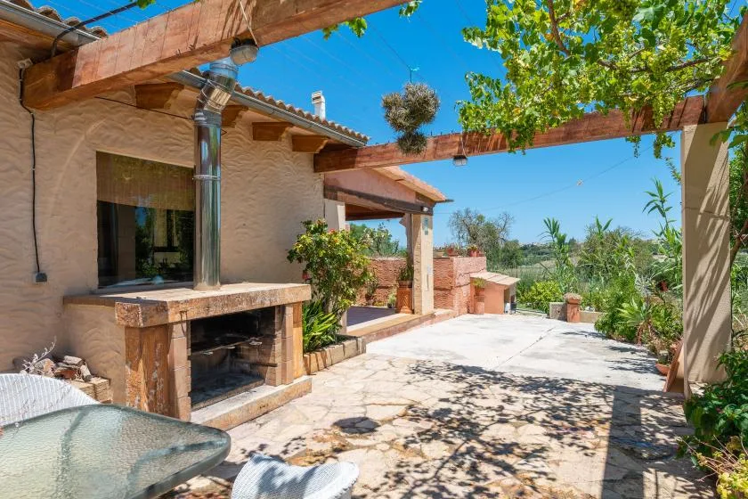 A sunlit stone patio beside a house, with a built-in outdoor fireplace.