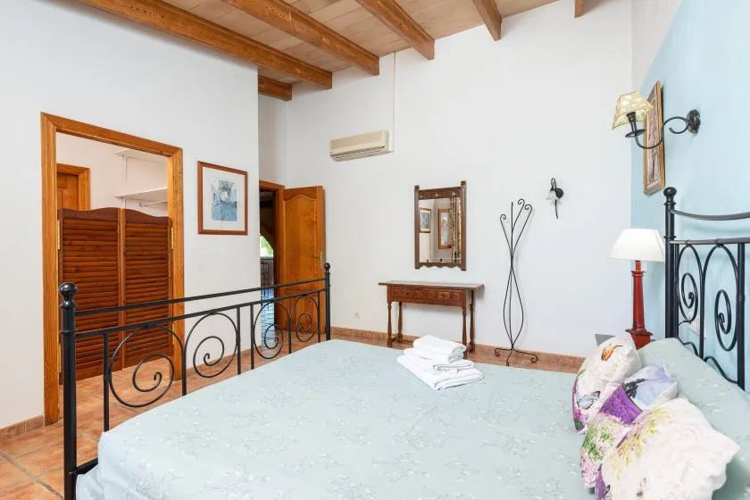 A bedroom with a bed, exposed wooden ceiling beams, and a black metal railing.
