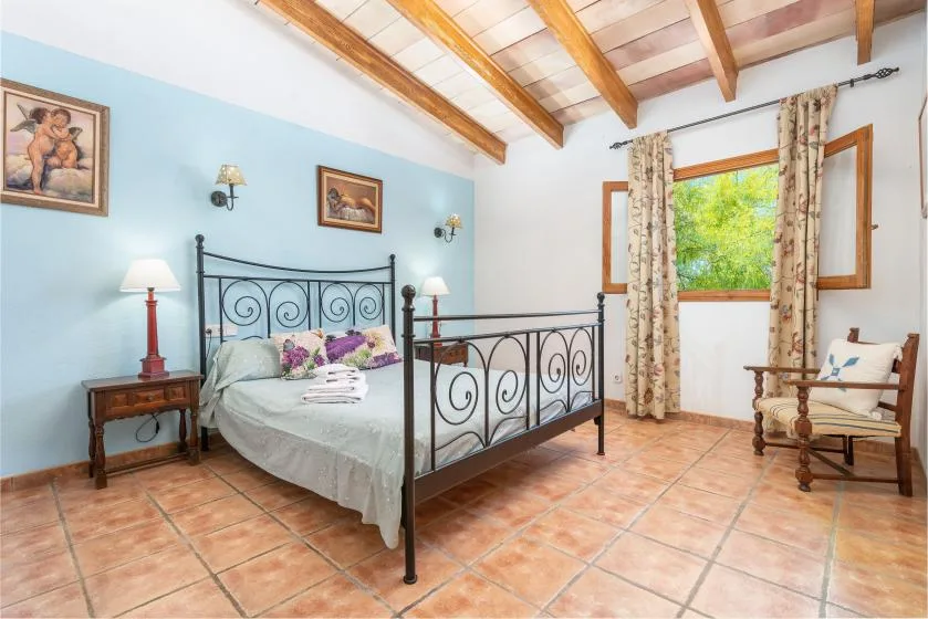 A bedroom with a metal bed, tiled floor, and a window overlooking greenery.