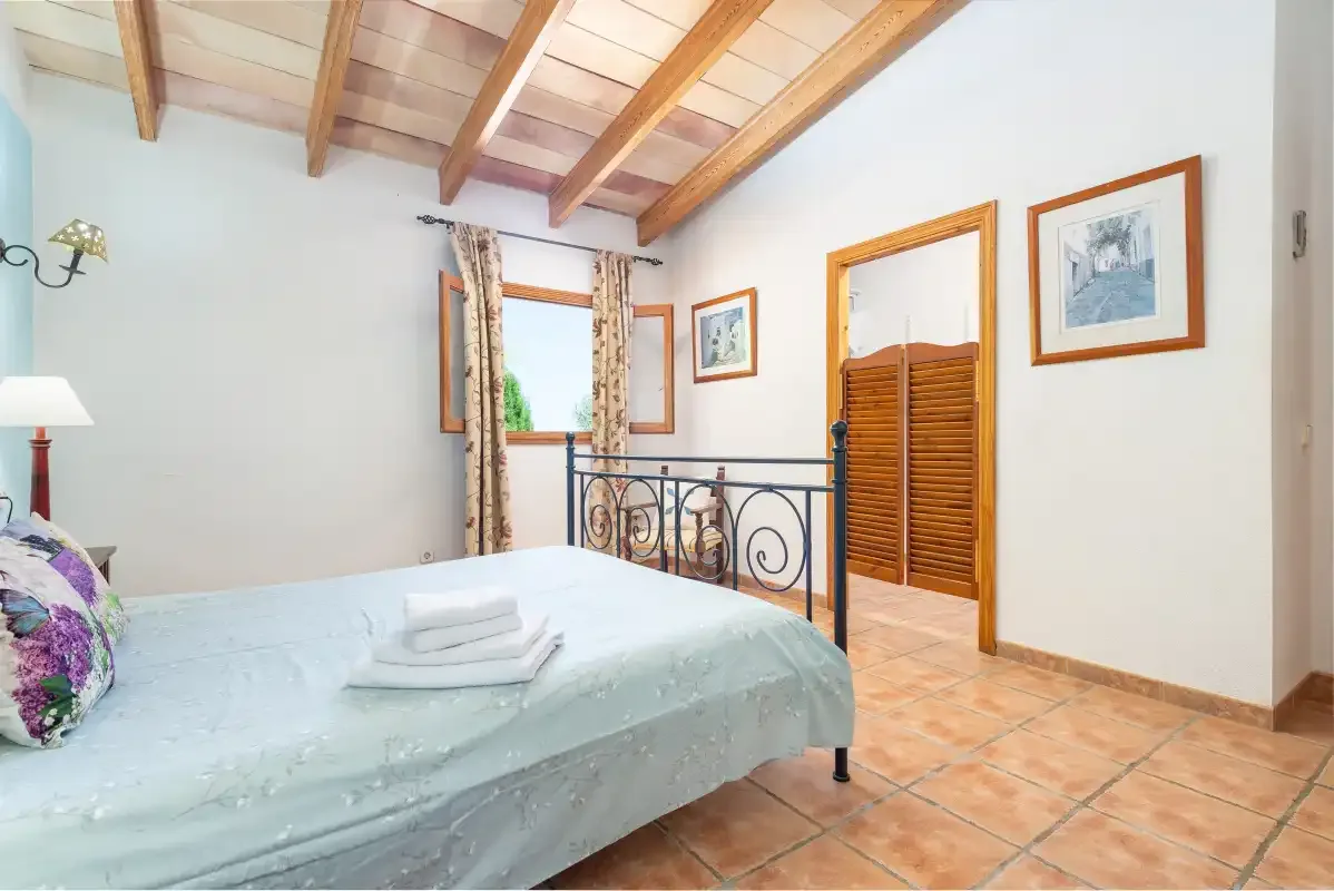 A bedroom with a bed, exposed wooden ceiling beams, and framed wall art.