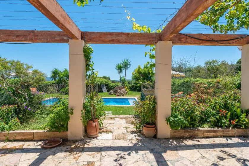 A garden patio opens onto a swimming pool, framed by wooden pergola beams.