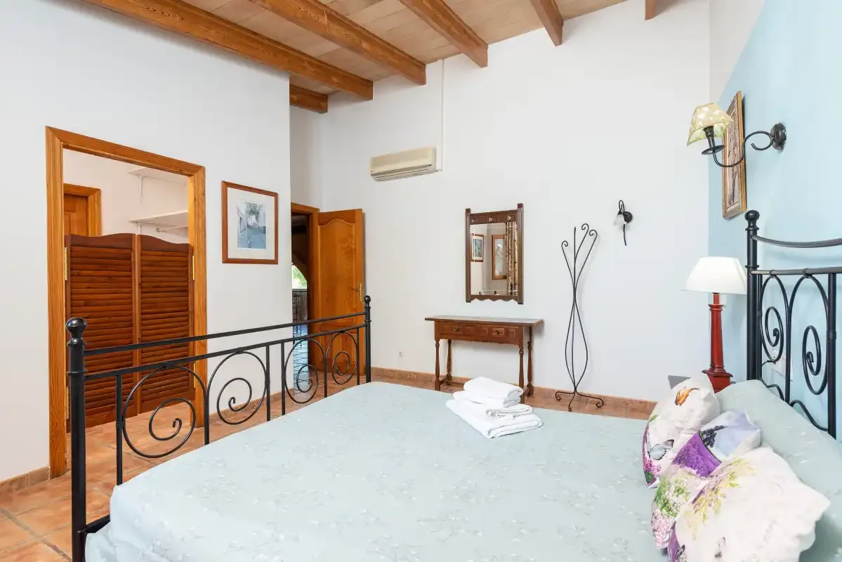 A bedroom with a bed, exposed wooden ceiling beams, and a small dressing table.