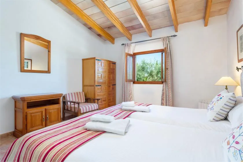 A bedroom with white bedding, striped bedspreads, and a wooden ceiling.