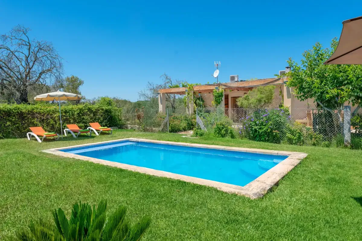An outdoor swimming pool sits in a grassy garden beside a house.