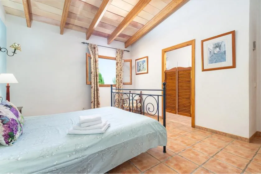 A bedroom with a bed, exposed wooden ceiling beams, and a window.
