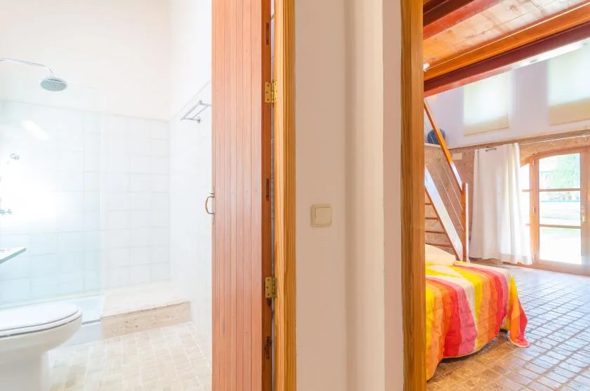 A bathroom opens onto a bedroom with colorful bedding and a wooden staircase.