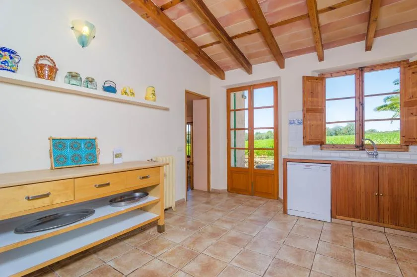 A bright kitchen with wooden cabinets, a countertop, and a window overlooking greenery.