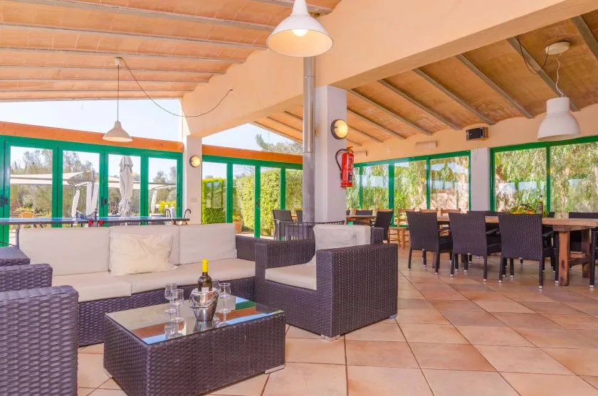 A covered patio dining and seating area has large windows and a tiled floor.