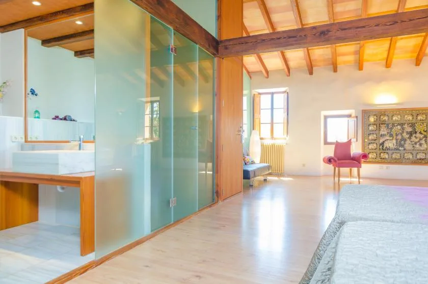 A bright bedroom with an adjoining glass-enclosed shower area and a bed.