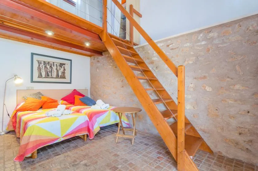 A colorful bedroom with two beds beneath a wooden loft and staircase.