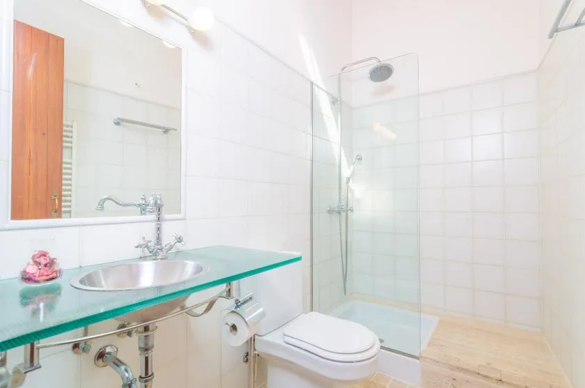A bright tiled bathroom with a glass shower and wall-mounted sink.